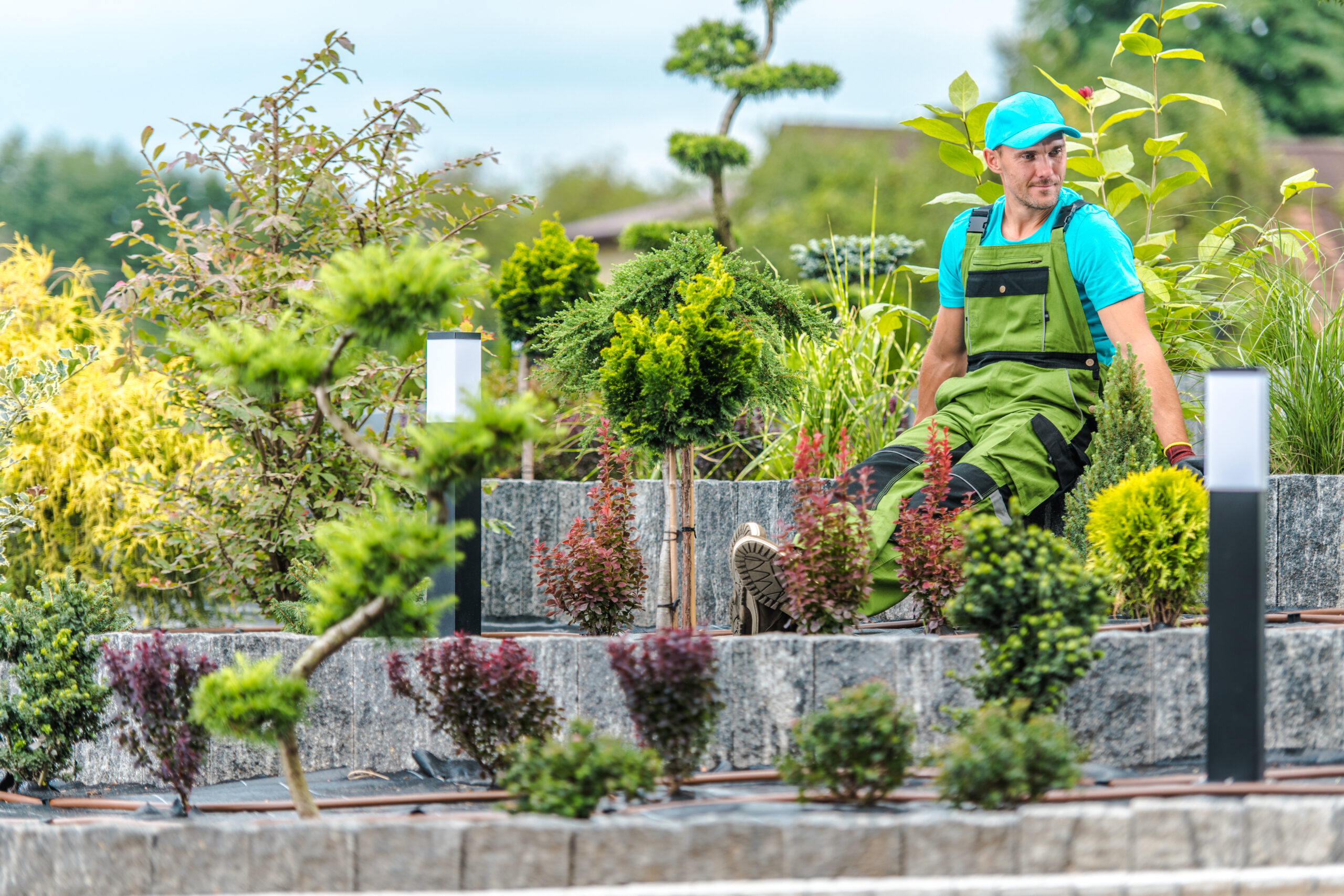 Caucasian Garden Worker Proudly Sitting in the Middle of Freshly Finished Island Garden Bed Enjoying the Results of His Landscape Design Work.