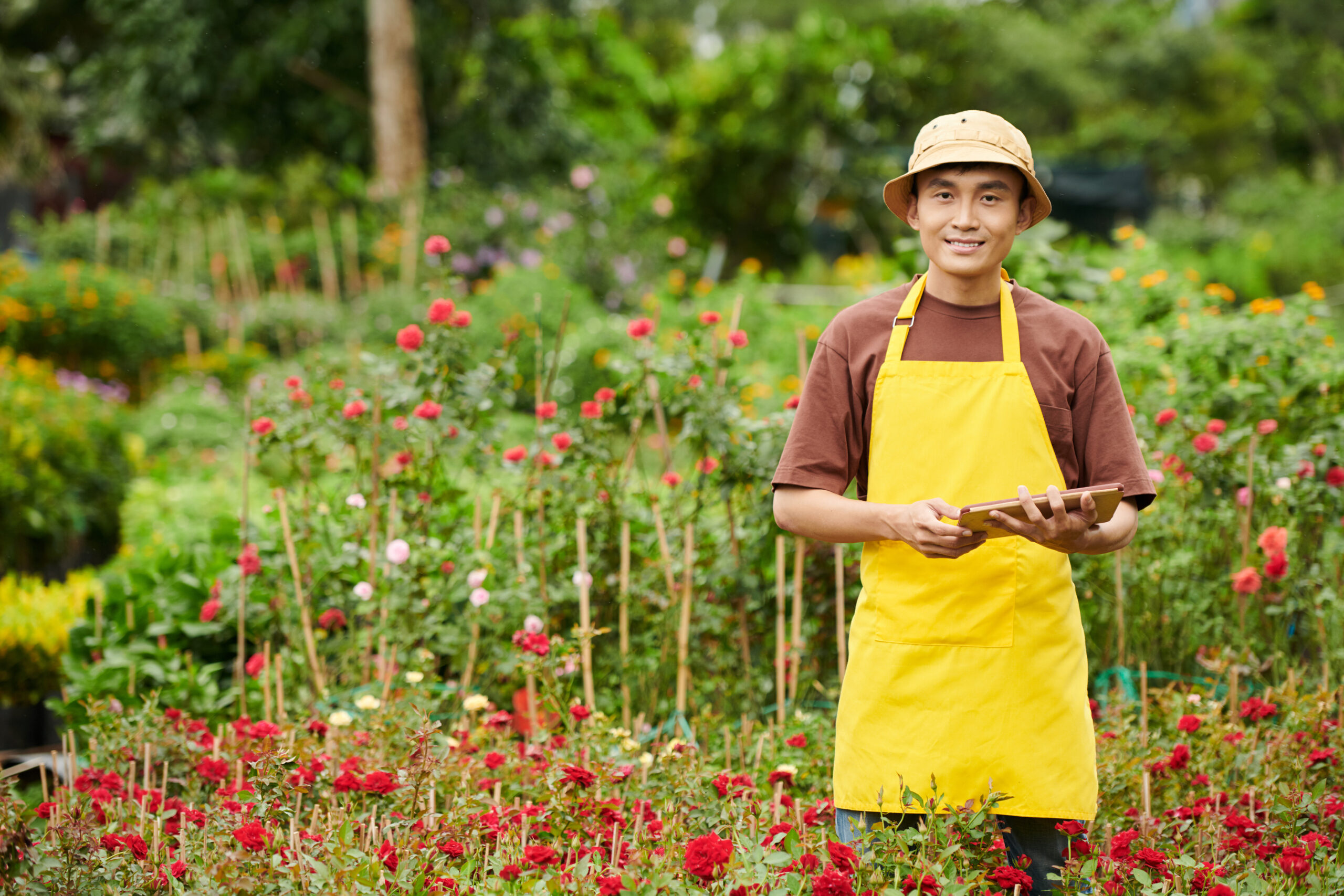 Portrait of plant nursery owner with digital tablet checking quality of blooming roses
