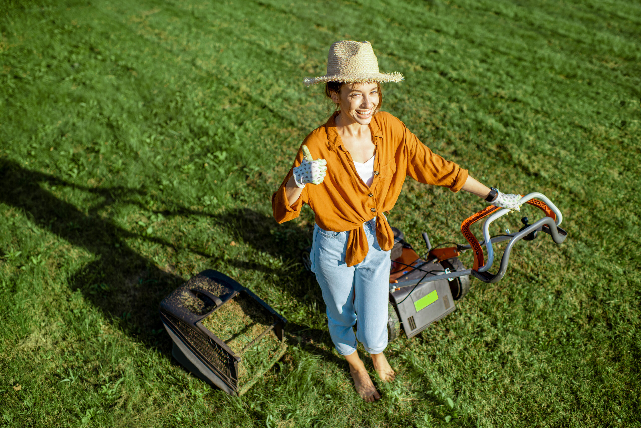 Portrait of a beautiful young woman dressed casually resting while cutting grass with lawn mower on the backyard